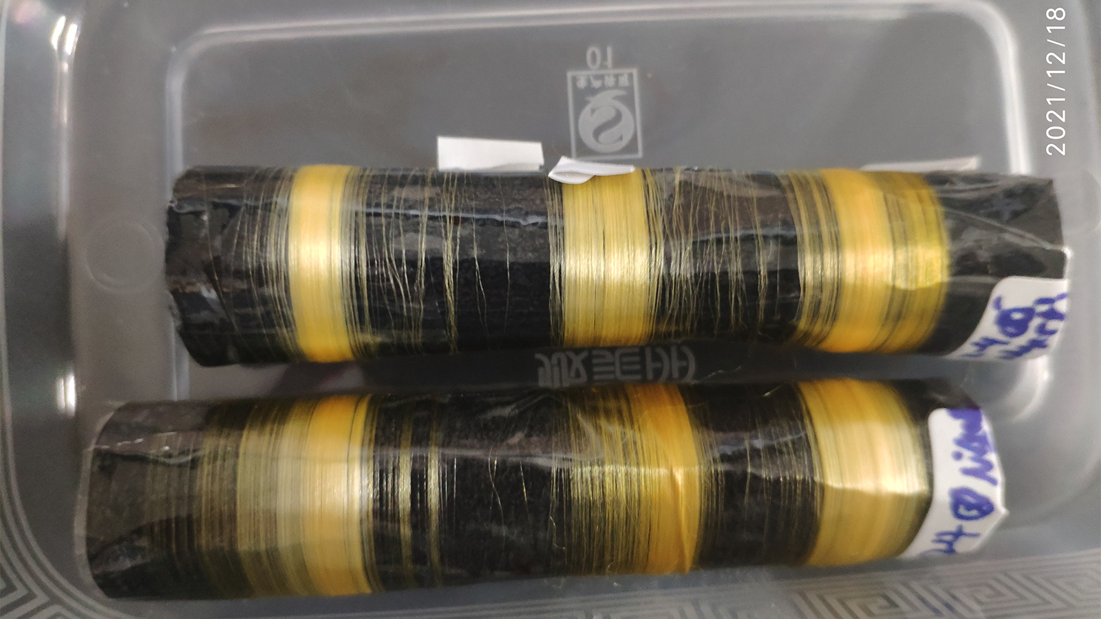 Two black and yellow strips of string in a plastic container.